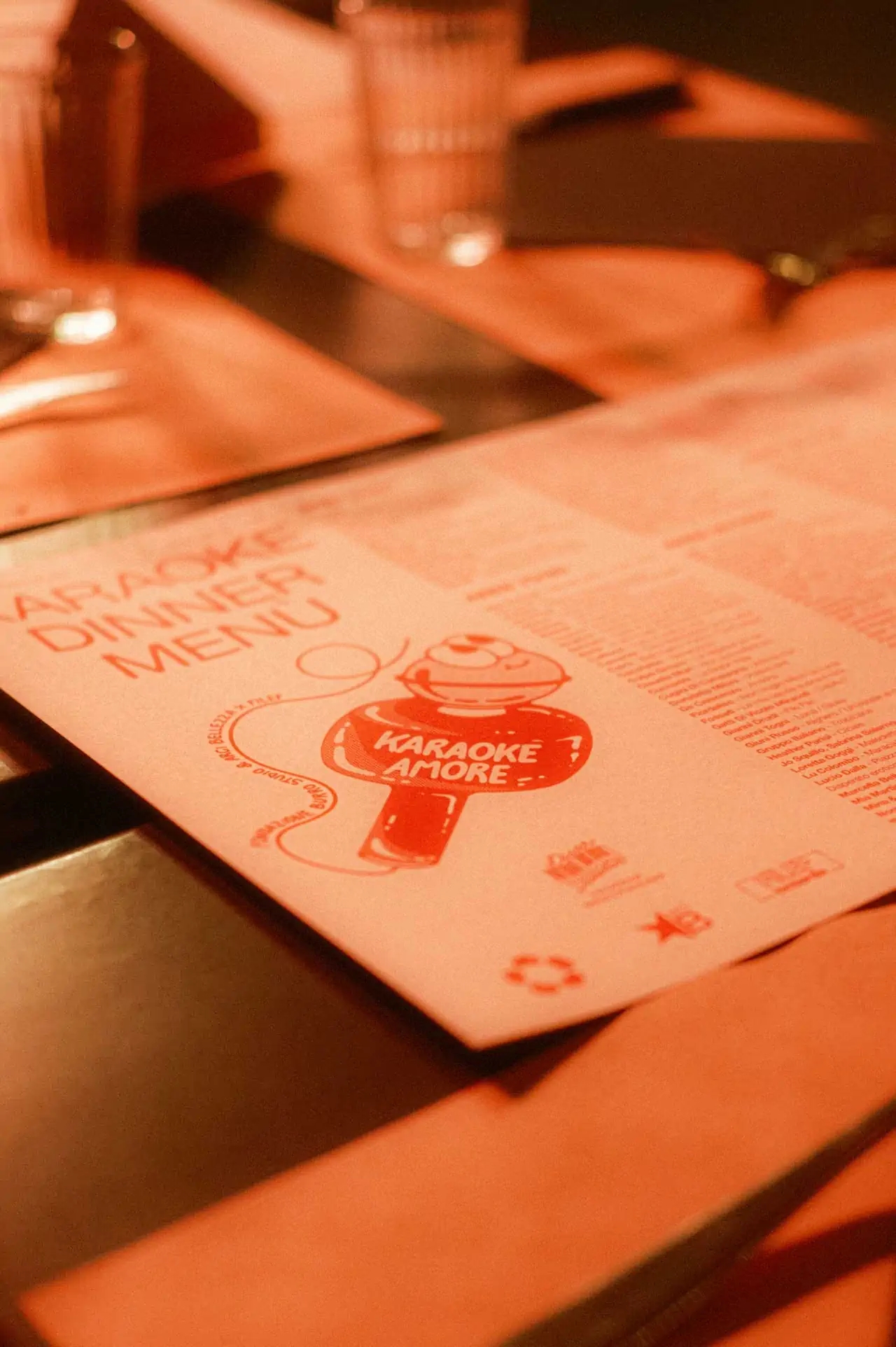 Detail of a white light cardboard paper menu printed in orange, which is laid on a dinner table, in a soft light.